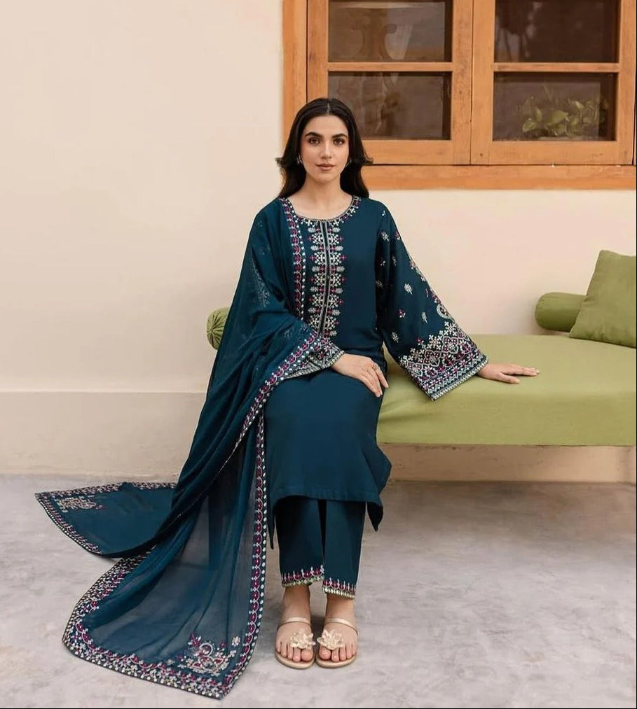 Woman in a teal traditional outfit sitting on a green couch with a wooden window in the background.